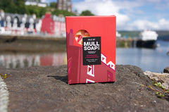 A mandarin and cranberry scented soy wax melt. shown sitting on the pier in Tobermory bay next to the red house that inspired the 'red building' packaging design. Made by the Isle of Mull soap co 