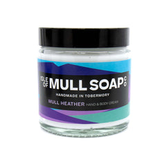 A glass jar with black lid. colourful purple label design, filled with mull heather hand and body cream handmade in Tobermory by the Isle of Mull soap co. 