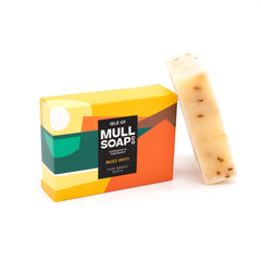 a buzz off insect repellent soap box sitting next to the soap bar. The box is bright orange green and yellow and says 'pure midget death' Handmade in Tobermory by the Isle of Mull soap co.  