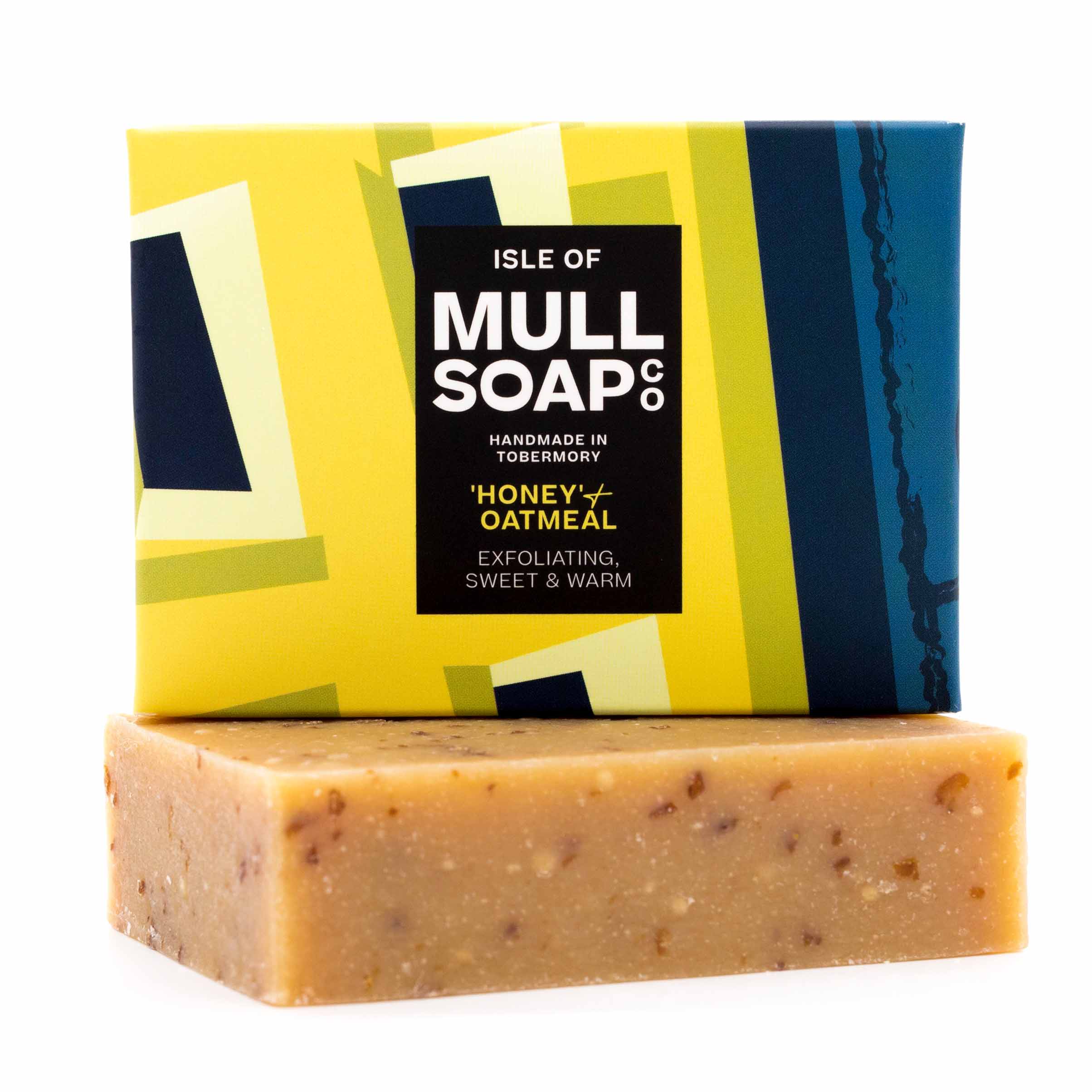 a vegan honey and oatmeal soap box sitting on top of the brown soap bar. The box is a blue and yellow design. The soap is described as exfoliating sweet and warm. Handmade in Tobermory by the Isle of Mull soap co.  