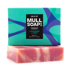 a lavender and mint soap box sitting on the swirled pink soap bar. The box is a blue and green design. The soap is described as bright, minted floral. Handmade in Tobermory by the Isle of Mull soap co.  