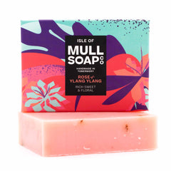 a rose and ylang ylang soap box sitting on the pink soap bar. The box is a pink and purple colourful floral design. The soap is described as rich, sweet and floral. Handmade in Tobermory by the Isle of Mull soap co.  