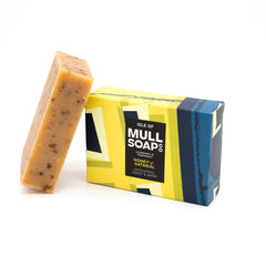 a vegan honey and oatmeal soap box sitting next to the brown soap bar. The box is a blue and yellow design. The soap is described as exfoliating sweet and warm. Handmade in Tobermory by the Isle of Mull soap co.  