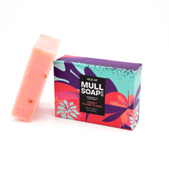 a rose and ylang ylang soap box sitting next to the pink soap bar. The box is a pink and purple colourful floral design. The soap is described as rich, sweet and floral. Handmade in Tobermory by the Isle of Mull soap co.  